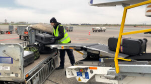 Ground handling staff safely loading baggage onto an aircraft using the Power Stow Tail Loader, reducing manual lifting and injury risks.